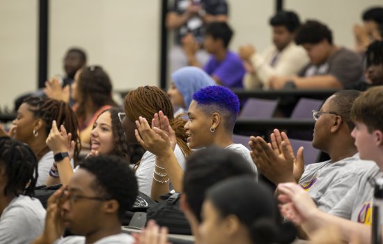 Students seated together in a lecture hall smile and applaud