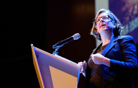 Virginia Eubanks, in glasses and a blue jacket, speaks at a microphone at a podium