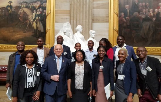 A group of smiling people pose inside the U.S. Capital in front of a sculpture and two paintings