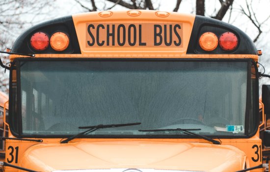 A close-up image of a yellow school bus with a rain-streaked windshield surrounded by other buses.