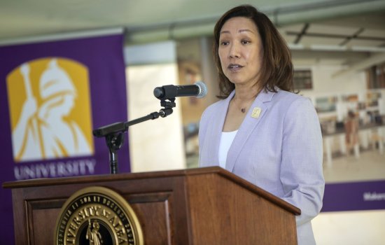 Provost Carol Kim, in a white shirt and pale purple jacket, stands at a microphone at a lecturn with the University at Albany seal on it.