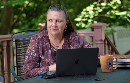 CEAS Dean Michele J. Grimm sits at a table outdoors with a laptop in front of her and a coffee mug.