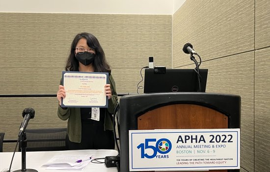 Fei Tang stands behind a podium, holding up a certificate.