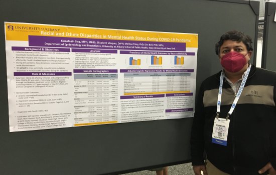 Kamalnain Siag stands next to a poster describing his research. He wears a red face mask.