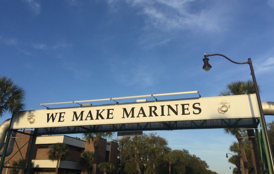 Sun illuminates a sign that reads "WE MAKE MARINES" against a backdrop of blue sky and palm trees in Parris Island, South Carolina.