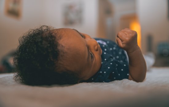 Baby wearing a dark shirt with star pattern reclines on a white, furry blanket. 