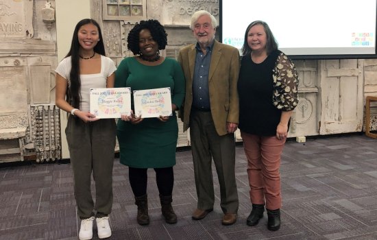 Four smiling people stand in a row, two holding certificates