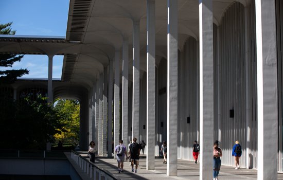 The School of Education is housed within Catskill, a building among those on the Academic Podium. Here, students are shown walking in front of Catskill on a clear, sunny day.