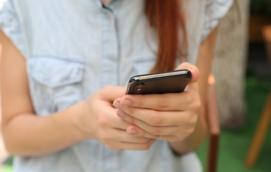 Woman in blue button down shirt holds her cell phone.