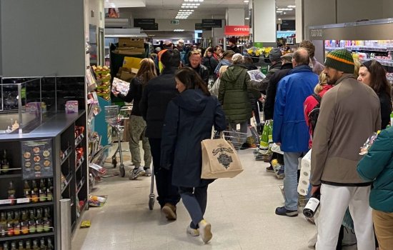 People stand in line holding their goods, waiting to check out of a grocery store.
