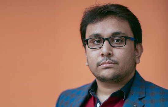 Jayanta Talukder stands in front of a soft orange background