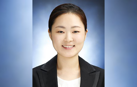 Kyoungah Noh smiles in a black blazer in front of a blue background