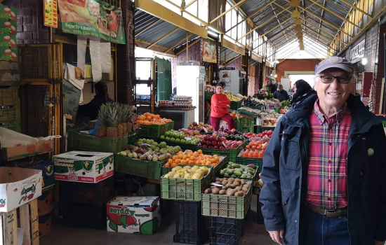 a man stands indoors in front of fresh fruit at a farmer's market in Santiago, Chile.