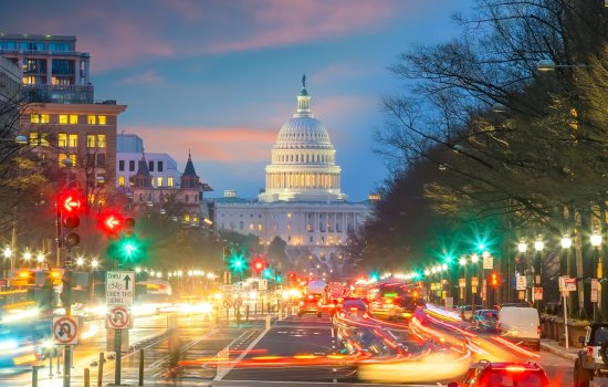 The U.S. Capitol building at dusk as cars with lights zoom by.