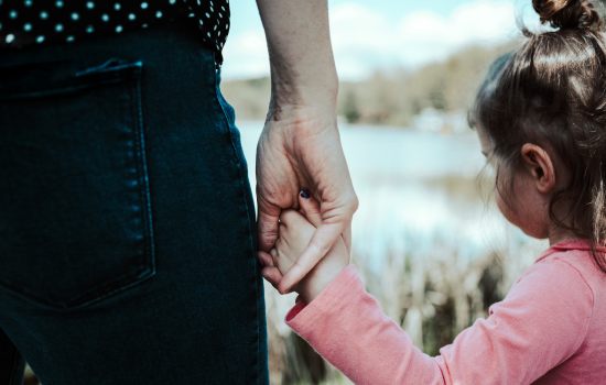 A woman holds a small child's hand.