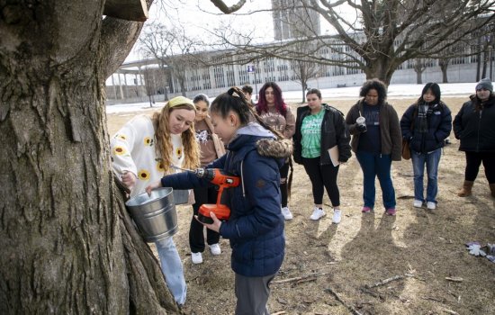 Olivia Dirla and Magnolia Roosa, from UAlbany's Office of Sustainability, demonstrate maple tree tapping for students at Dutch Quad.