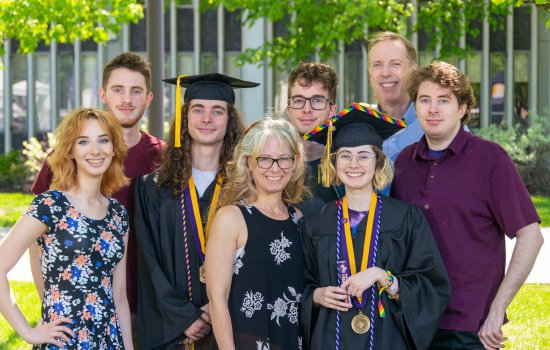 A family of six siblings and a mother and father celebrate commencement outdoors as two of the children where graduation regalia.