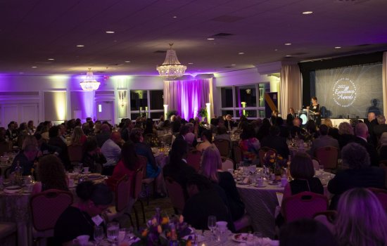 A room full of people at round tables set for dinner and adorned with purple and gold tulips