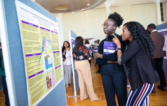 A student and a mentor look at a poster on a board at the School of Public Health's Poster Day.