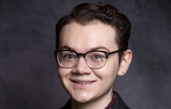 A young man with short brown hair and glasses smiles for a portrait.
