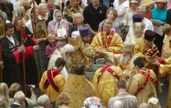 Orthodox Christians in gold ceremonial garb participate in the blessing of the water rite at St. Vladimir Memorial Church in Jackson, N.J. A crowd watches, some holding framed pictures.
