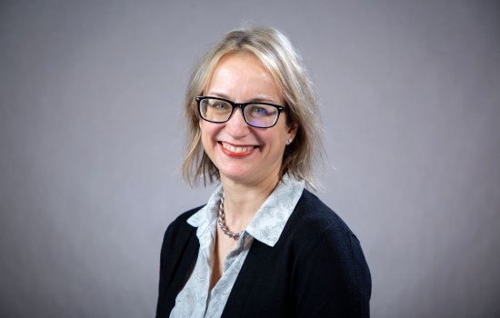 A woman with short blonde hair and glasses smiles for a portrait.