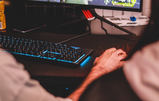 A hand hovers over a computer mouse next to a lit-up keyboard and computer screen.