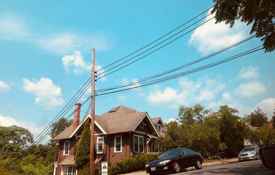 A black car in front of a brown house next to green trees.