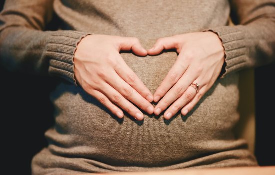 A women holds her hands over her pregnant stomach, creating a heart shape.