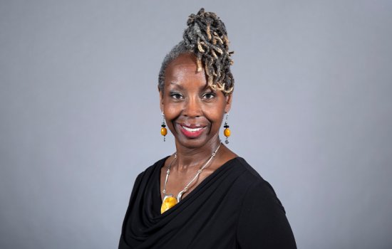 Professor Kyra Gaunt wearing a black blouse and yellow and silver earrings and a necklace, with her hair piled on top of her head.