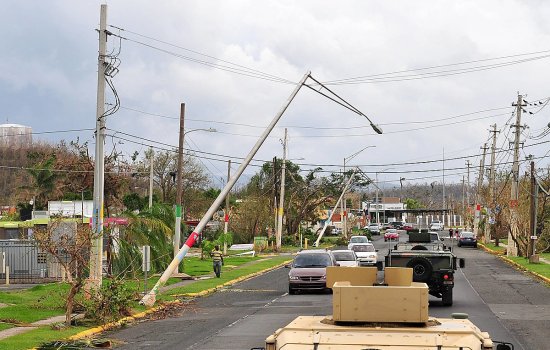 A convoy of military vehicles drive down a road in Puerto Rico with damaged power lines and light poles.