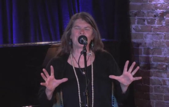 storyteller at mic performs with eyes closed and hands extended