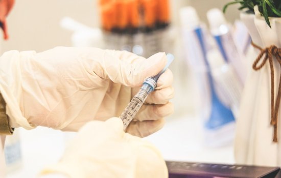 Hands wearing protective plastic gloves hold a syringe
