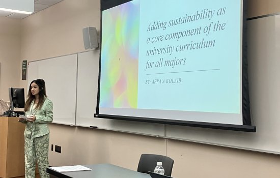 Afra'a presenting at UAlbany Showcase. She stands in front of a screen displaying her presentation.