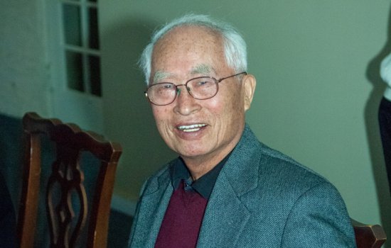 Pong S Lee sits at a table while wearing glasses, a burgundy pullover and grey suit jacket.