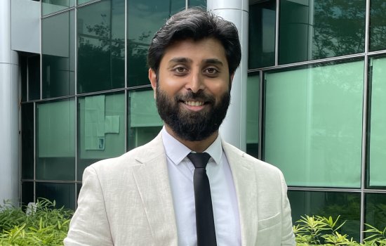 Arun Chandrasekaran wears a cream colored linen suit jacket and dark blue tie for a portrait outside the RNA Institute.