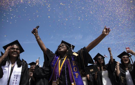 A group of cheering students at graduation wearing caps and gowns.