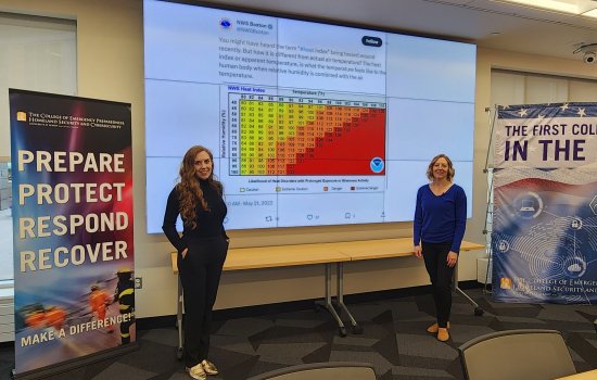 Micki Olson and Jeannette Sutton stand in front of a screen displaying a National Weather Service tweet at the CEHC Ops Command Center.