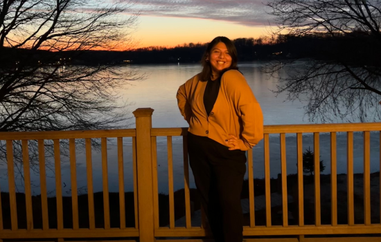 Sapphire Correa stands in front of a lake. The sun is setting behind the lake.