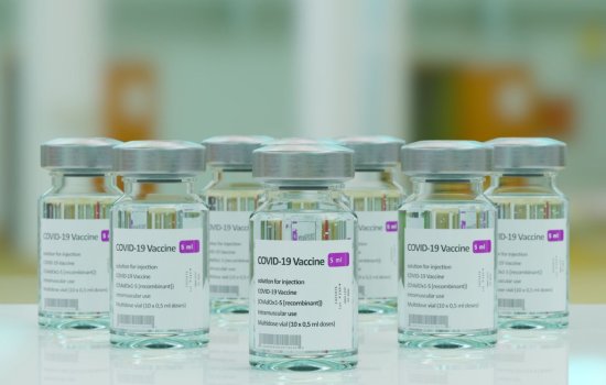 Seven bottles of the covid-19 vaccine are on a smooth white tabletop with blurred background.