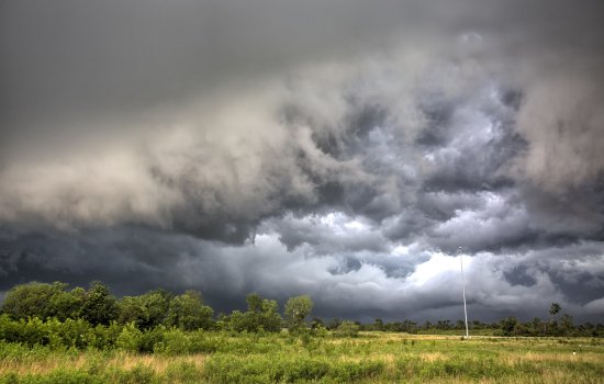 A fierce storm front with dark clouds passes over grassland.
