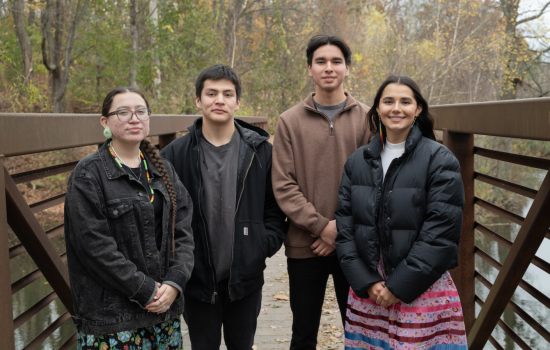 Two young men and two young women stand on a bridge over Parker Pond on the UAlbany campus on an overcast fall day.