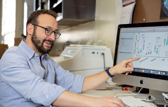 Paolo Forni smiles and points at a computer monitor displaying undreadable text.
