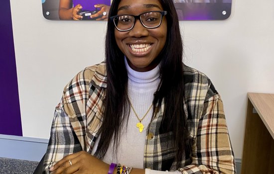 Maimouna Camara, a UAlbany MSW student, sits at a desk and smiles.
