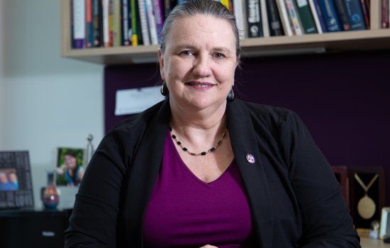 University at Albany’s College of Nanotechnology, Science, and Engineering (CNSE) Dean Michele J. Grimm sits at her desk with a row of books behind her.