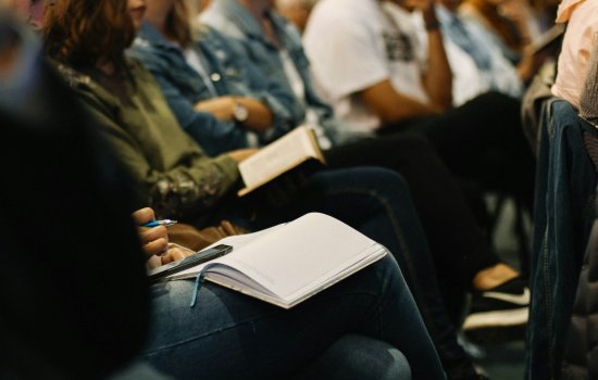 Closeup of seated people crowded in rows, with open notepads and books on their laps.