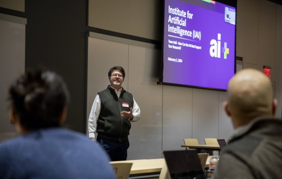 Eric Stern stands under a projection screen with the words “Institute for Artificial Intelligence” as he speaks to people seated in front of him.