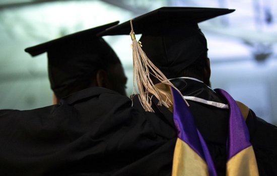 The backs of two graduates are seen in silhouette wearing mortorboards and graduation regalia