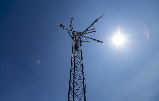 The sun shines behind the top of a New York Mesonet station weather tower.
