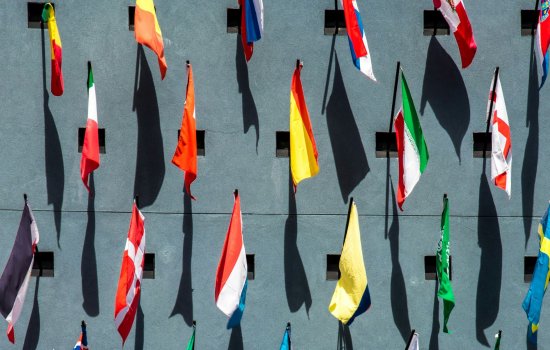 Flags of many nations, shot from above, with their shadows on a blue-gray background